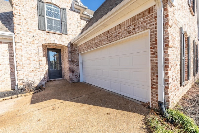 property entrance featuring brick siding, concrete driveway, and a shingled roof