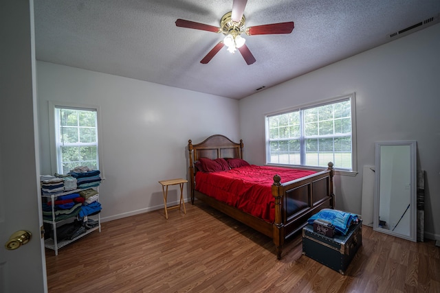 bedroom featuring visible vents, a textured ceiling, baseboards, and wood finished floors