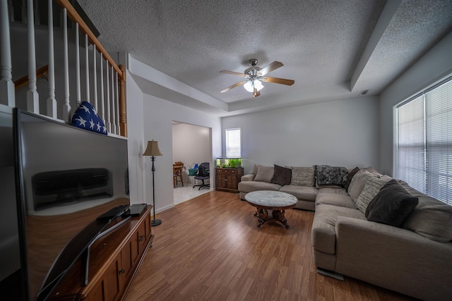 living room with visible vents, a textured ceiling, wood finished floors, a raised ceiling, and ceiling fan