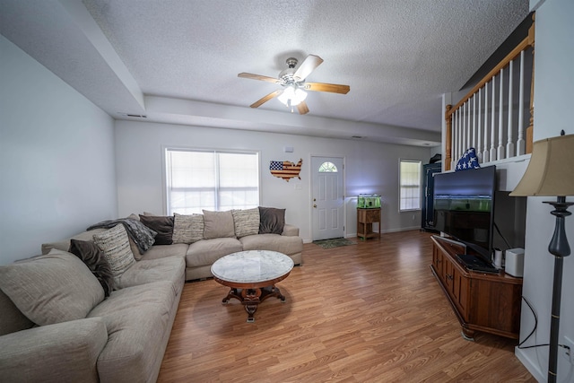 living room featuring a ceiling fan, baseboards, light wood finished floors, and a textured ceiling