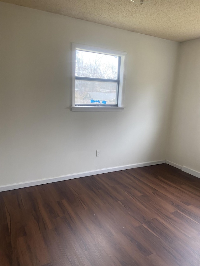 spare room featuring dark wood finished floors, a textured ceiling, and baseboards