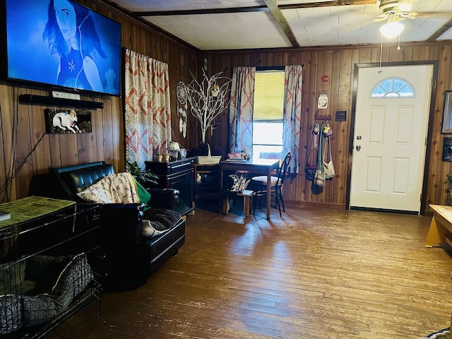 interior space featuring wooden walls, a ceiling fan, wood finished floors, baseboards, and beamed ceiling