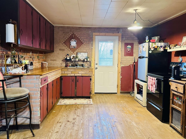 kitchen with black / electric stove, brick wall, a sink, light countertops, and light wood-style floors