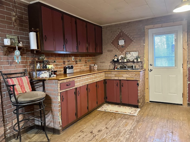 kitchen with brick wall, light wood-style flooring, a sink, light countertops, and crown molding