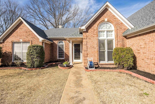 view of front of property with a front yard, brick siding, and a shingled roof