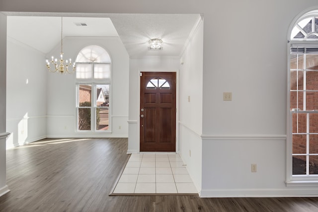 foyer entrance with wood finished floors, baseboards, visible vents, ornamental molding, and a chandelier