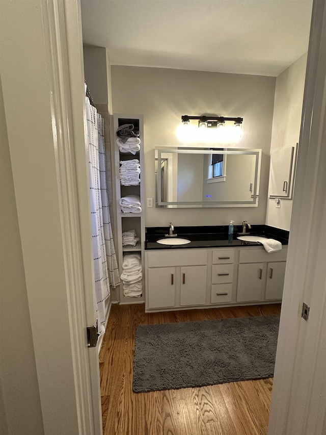 full bathroom with double vanity, wood finished floors, a shower with curtain, and a sink