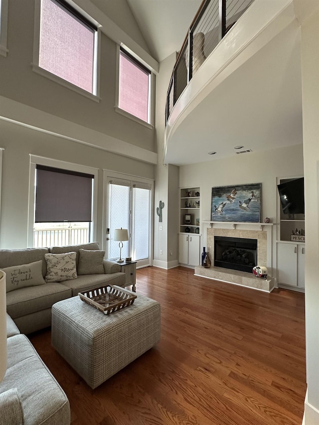 living area featuring built in shelves, baseboards, vaulted ceiling, a fireplace, and wood finished floors