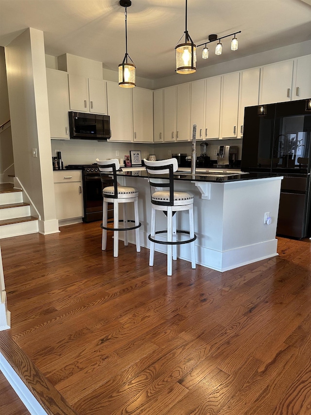 kitchen featuring dark wood-type flooring, black appliances, a kitchen breakfast bar, dark countertops, and white cabinetry