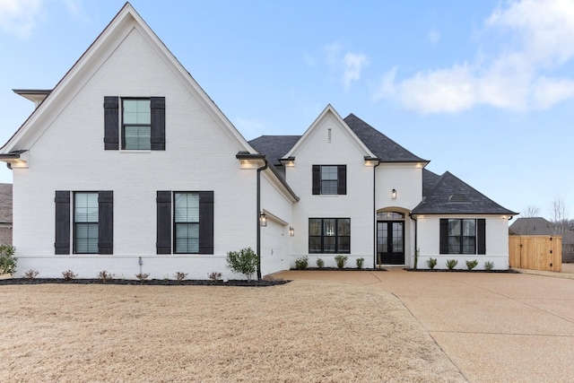 french provincial home featuring brick siding, a garage, and fence