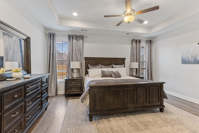 bedroom with a tray ceiling, baseboards, visible vents, and light wood finished floors