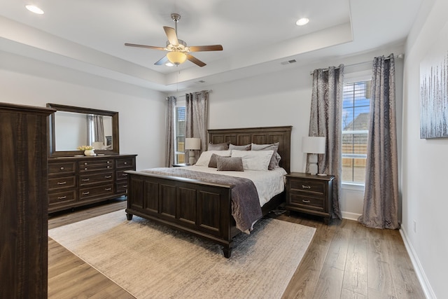 bedroom with visible vents, a raised ceiling, baseboards, and wood finished floors