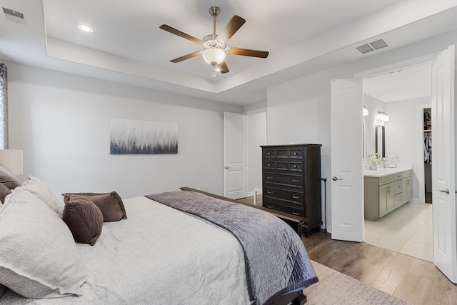 bedroom with ceiling fan, visible vents, a raised ceiling, and wood finished floors