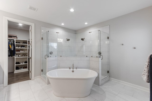 bathroom with a walk in closet, a shower stall, visible vents, and a freestanding bath