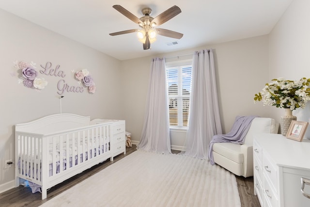 bedroom with ceiling fan, baseboards, a nursery area, and wood finished floors