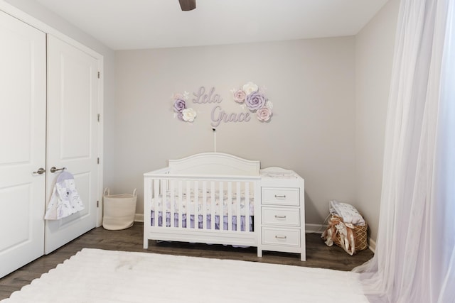 bedroom with dark wood finished floors, ceiling fan, a crib, and baseboards