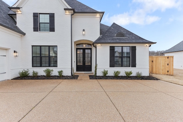 french country home featuring a garage, french doors, brick siding, and a shingled roof