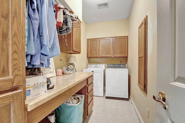 laundry area featuring washing machine and clothes dryer, visible vents, light tile patterned floors, cabinet space, and a textured ceiling