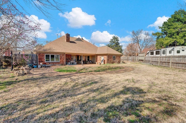 back of property featuring brick siding, a yard, a chimney, and a fenced backyard