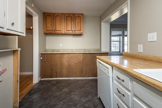 kitchen with brown cabinetry, baseboards, white dishwasher, and light countertops