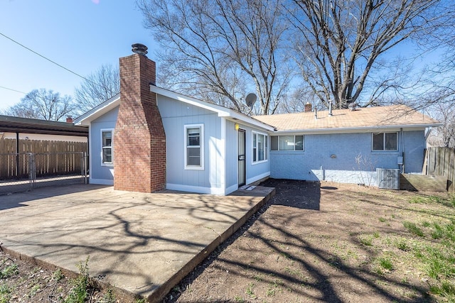 back of house featuring fence, driveway, central AC, a chimney, and brick siding