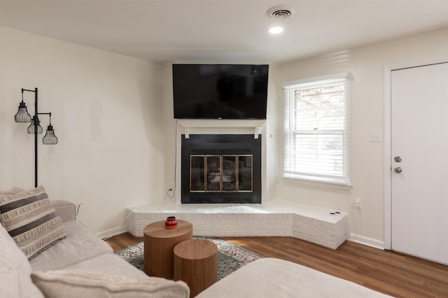 living area featuring visible vents, baseboards, a glass covered fireplace, and wood finished floors