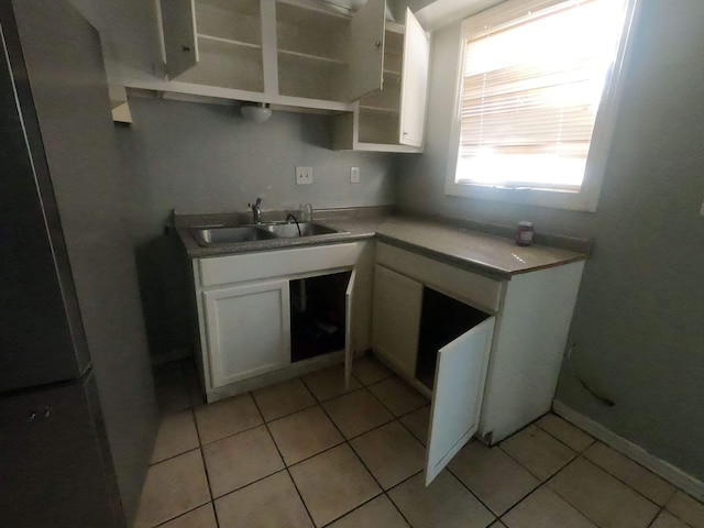 kitchen with a sink, white cabinets, light tile patterned flooring, and freestanding refrigerator