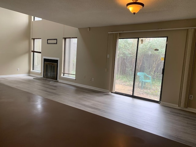 unfurnished living room featuring a fireplace with flush hearth, wood finished floors, baseboards, and a textured ceiling