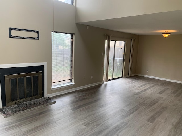 unfurnished living room featuring a wealth of natural light, baseboards, wood finished floors, and a glass covered fireplace