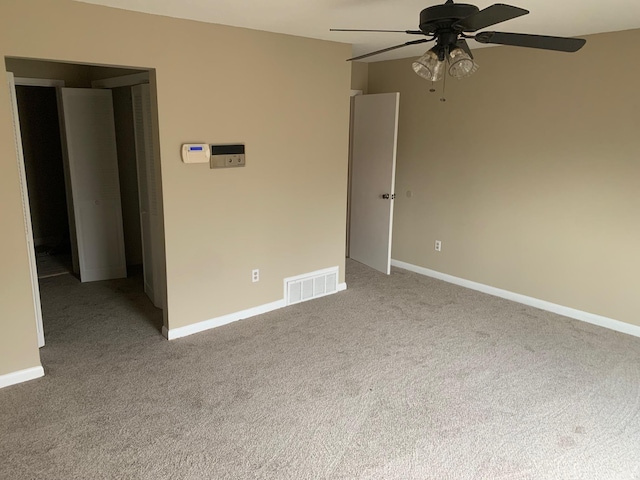 empty room with visible vents, light colored carpet, a ceiling fan, and baseboards