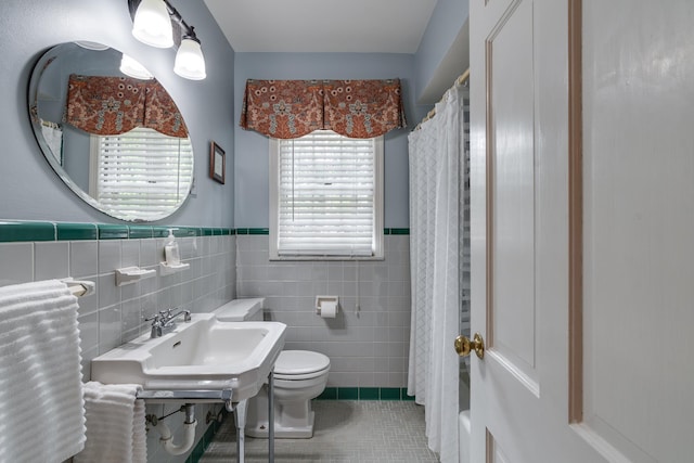 full bath featuring tile patterned floors, toilet, curtained shower, tile walls, and wainscoting