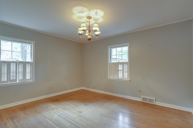 empty room with visible vents, ornamental molding, wood finished floors, baseboards, and a chandelier