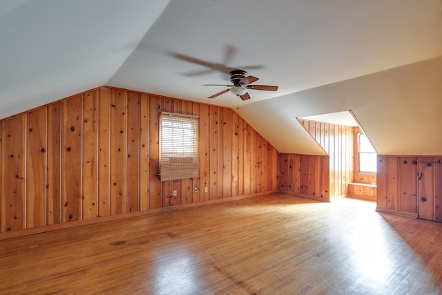 additional living space featuring lofted ceiling, light wood-type flooring, wood walls, and ceiling fan