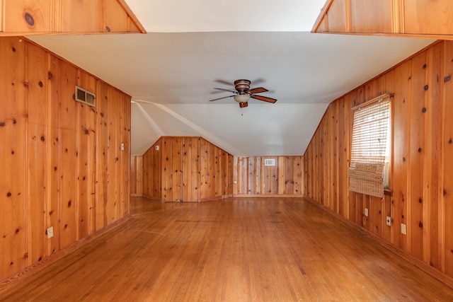 bonus room with a ceiling fan, visible vents, light wood-style flooring, vaulted ceiling, and wood walls