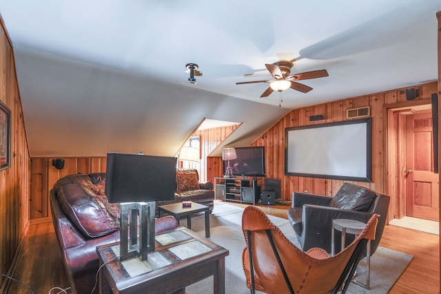 living room with visible vents, wood finished floors, wood walls, lofted ceiling, and ceiling fan