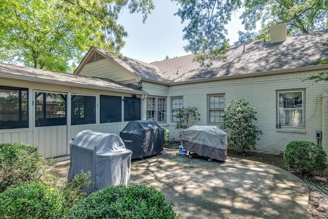 exterior space featuring roof with shingles, brick siding, a sunroom, and a chimney