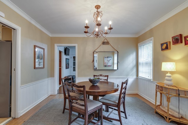 dining room featuring a wainscoted wall, a chandelier, ornamental molding, and light wood finished floors