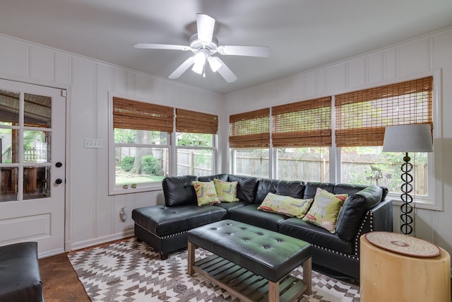 living area with ceiling fan, ornamental molding, and a decorative wall