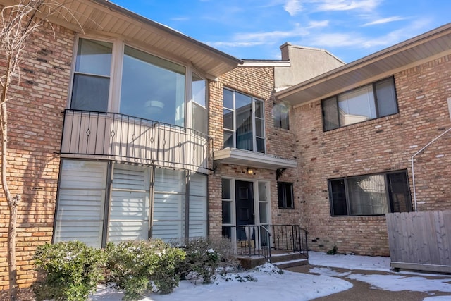 snow covered house featuring brick siding and a balcony