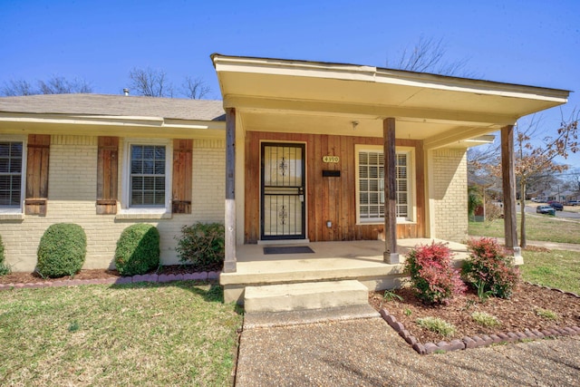 property entrance with a yard, brick siding, and covered porch