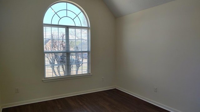 spare room featuring lofted ceiling, a healthy amount of sunlight, dark wood-style flooring, and baseboards