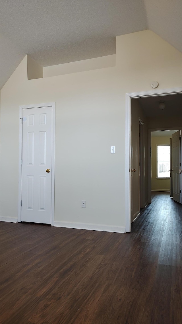 unfurnished room featuring dark wood finished floors, vaulted ceiling, and baseboards