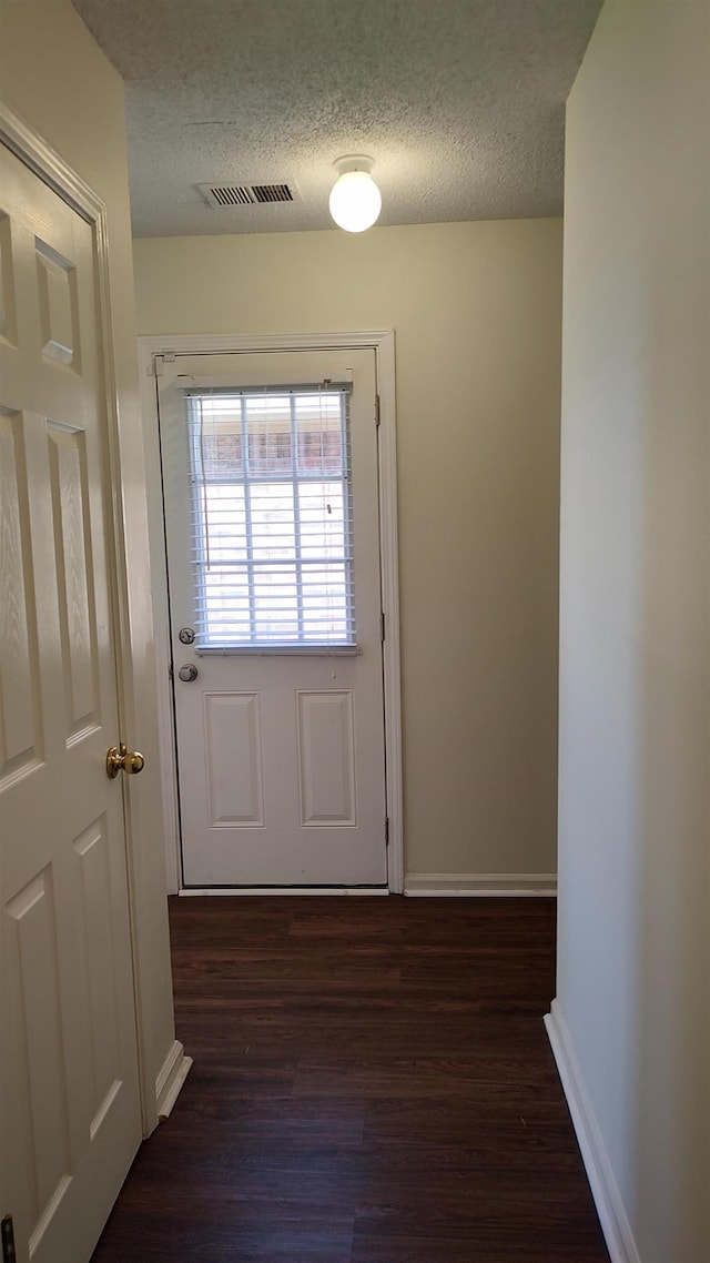 doorway featuring visible vents, a textured ceiling, dark wood-type flooring, and baseboards