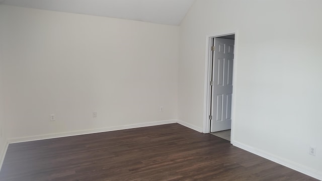 spare room with baseboards, dark wood-style floors, and vaulted ceiling