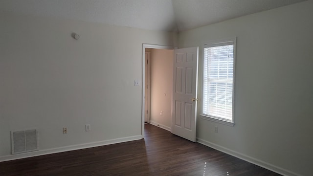 spare room featuring visible vents, lofted ceiling, baseboards, and dark wood-style floors