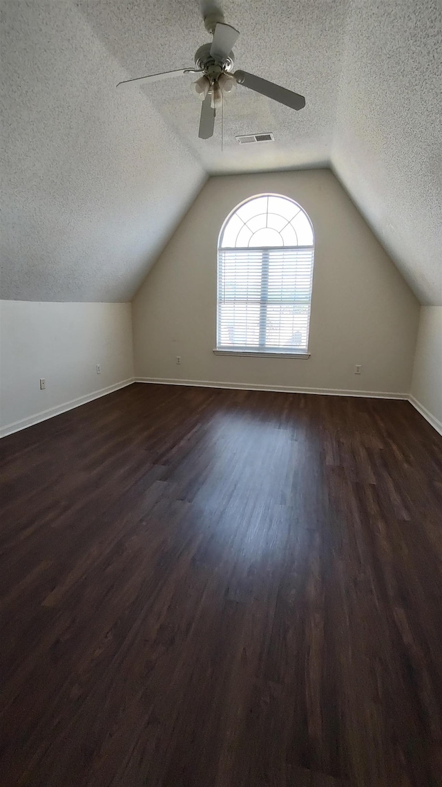 additional living space with visible vents, lofted ceiling, a textured ceiling, and dark wood finished floors