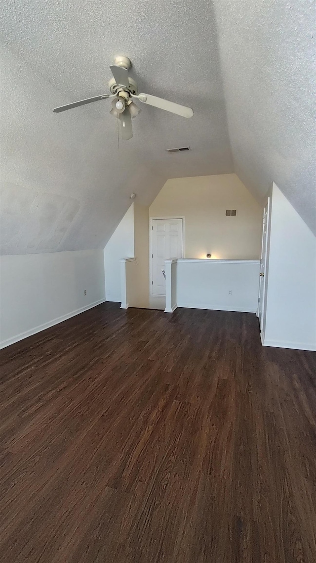 additional living space featuring vaulted ceiling, dark wood-style floors, visible vents, and a textured ceiling