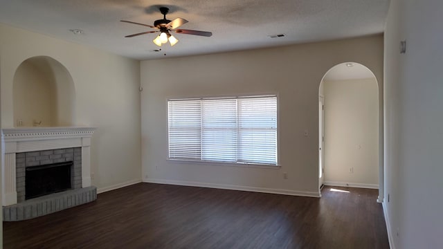 unfurnished living room featuring baseboards, visible vents, dark wood finished floors, ceiling fan, and a brick fireplace