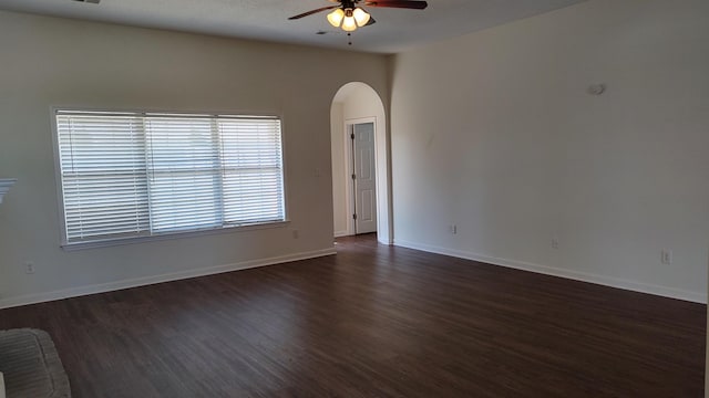 unfurnished room with arched walkways, dark wood-style floors, baseboards, and ceiling fan