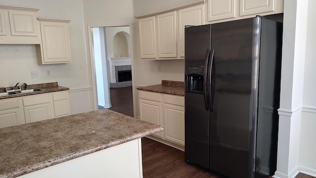 kitchen featuring dark wood-style floors, a sink, a brick fireplace, and black refrigerator with ice dispenser